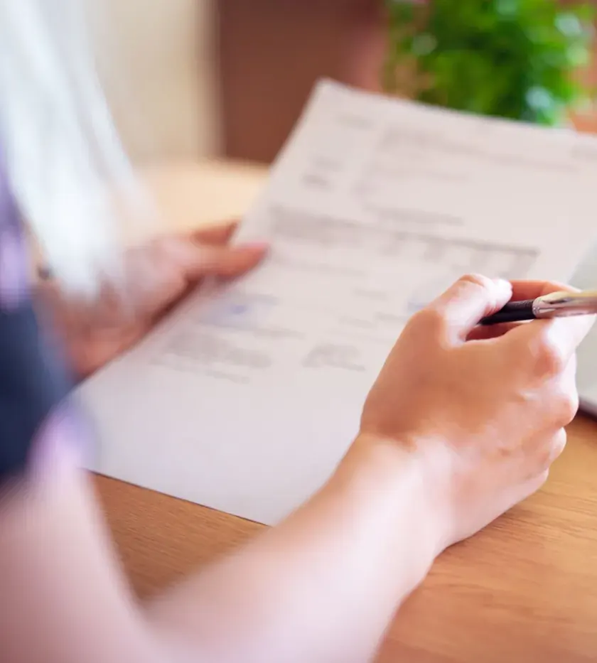 A hand holding an order form beside a laptop